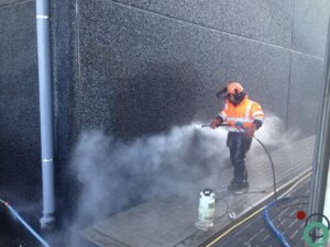 Medewerker van Chemifor bezig met het verwijderen van asfalt van een betonnen muur.