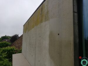 Betongevel met duidelijke mos- en algengroei, deels gereinigd voor contrast
