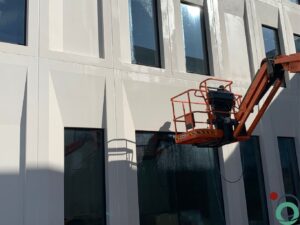 Gevelreiniging op hoogte met een hoogtewerker op een lichtkleurige betonstructuur