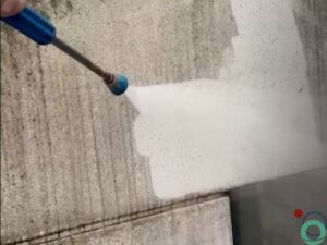 Hogedrukstraal verwijdert zwarte aanslag van betonnen muur met duidelijk kleurverschil tussen schoon en vuil oppervlak
