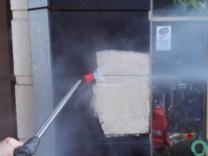 Zwartgeworden gevelsteen wordt plaatselijk gereinigd met hogedrukstraal waardoor de oorspronkelijke lichte kleur weer zichtbaar wordt