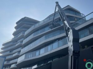 Modern appartementsgebouw met afgeronde glazen balustrades tijdens gevelreiniging met een hoogwerker