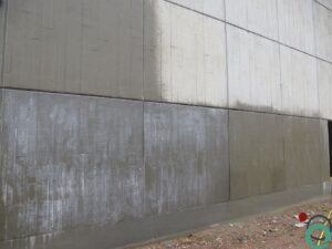 Gedeeltelijk gereinigde betonnen gevel met zichtbare overgang tussen vervuilde en schone zones