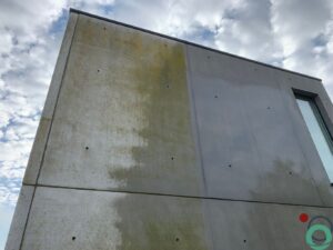 Moderne betonmuur met gele en groene vervuiling, waarvan de rechterzijde al gereinigd is