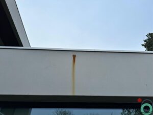Roestvlek op witte betonnen gevel onder een metalen bevestigingspunt
