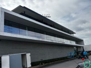 Een modern gebouw met grote glaspartijen en witte betonranden toont zichtbare vervuiling en zwarte aanslag onder de balustrade op elke verdieping.