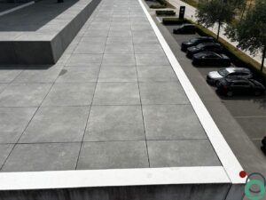 Dakterras met grote grijze tegels na een grondige reiniging, met uitzicht op geparkeerde auto's en een nette omgeving.