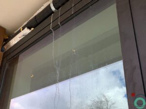 Witte kalk- en cementsporen zichtbaar op een zwart aluminium raamprofiel
