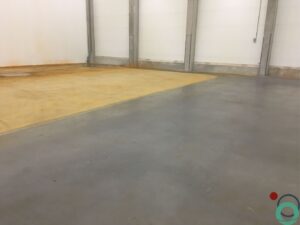 Uitgespreid roestwater veroorzaakt brede oranjebruine verkleuringen op een betonnen vloer in een industriële ruimte