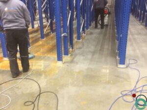 Uitgespreid roestwater veroorzaakt brede oranjebruine verkleuringen op een betonnen vloer in een industriële ruimte