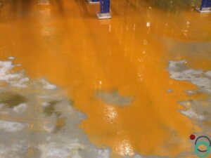 Uitgespreid roestwater veroorzaakt brede oranjebruine verkleuringen op een betonnen vloer in een industriële ruimte