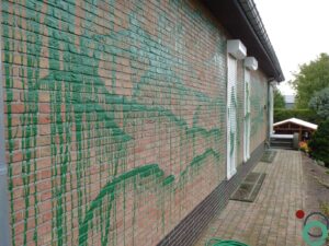 Groene verfspetters en druipers op een bakstenen muur en bestrating