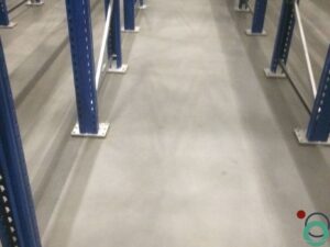 Uitgespreid roestwater veroorzaakt brede oranjebruine verkleuringen op een betonnen vloer in een industriële ruimte