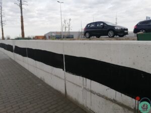 Zichtbetonnen keermuur vervuild met zwarte bitumenstroken die langs de wand uitlopen