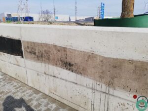 Zichtbetonnen keermuur vervuild met zwarte bitumenstroken die langs de wand uitlopen