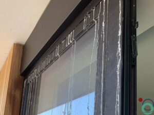 Witte kalk- en cementsporen zichtbaar op een zwart aluminium raamprofiel
