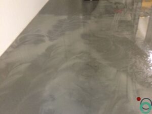 Uitgespreid roestwater veroorzaakt brede oranjebruine verkleuringen op een betonnen vloer in een industriële ruimte