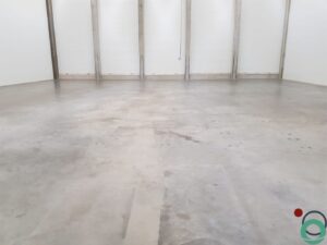 Uitgespreid roestwater veroorzaakt brede oranjebruine verkleuringen op een betonnen vloer in een industriële ruimte