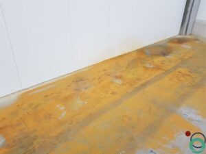 Uitgespreid roestwater veroorzaakt brede oranjebruine verkleuringen op een betonnen vloer in een industriële ruimte