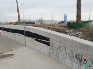Zichtbetonnen keermuur vervuild met zwarte bitumenstroken die langs de wand uitlopen