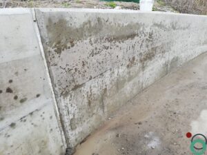 Zichtbetonnen keermuur vervuild met zwarte bitumenstroken die langs de wand uitlopen